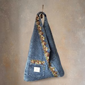 Front view of the hand-embellished denim wrap bag with green floral lace hanging on a wall hook.