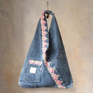 Front view of denim wrap bag with pink floral lace hanging from a hook.