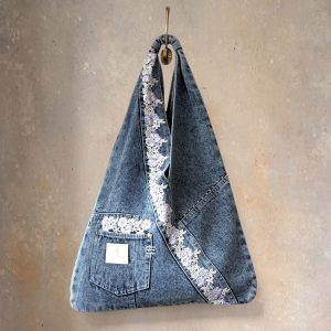 Front view of denim wrap bag with purple floral lace hanging from a hook.