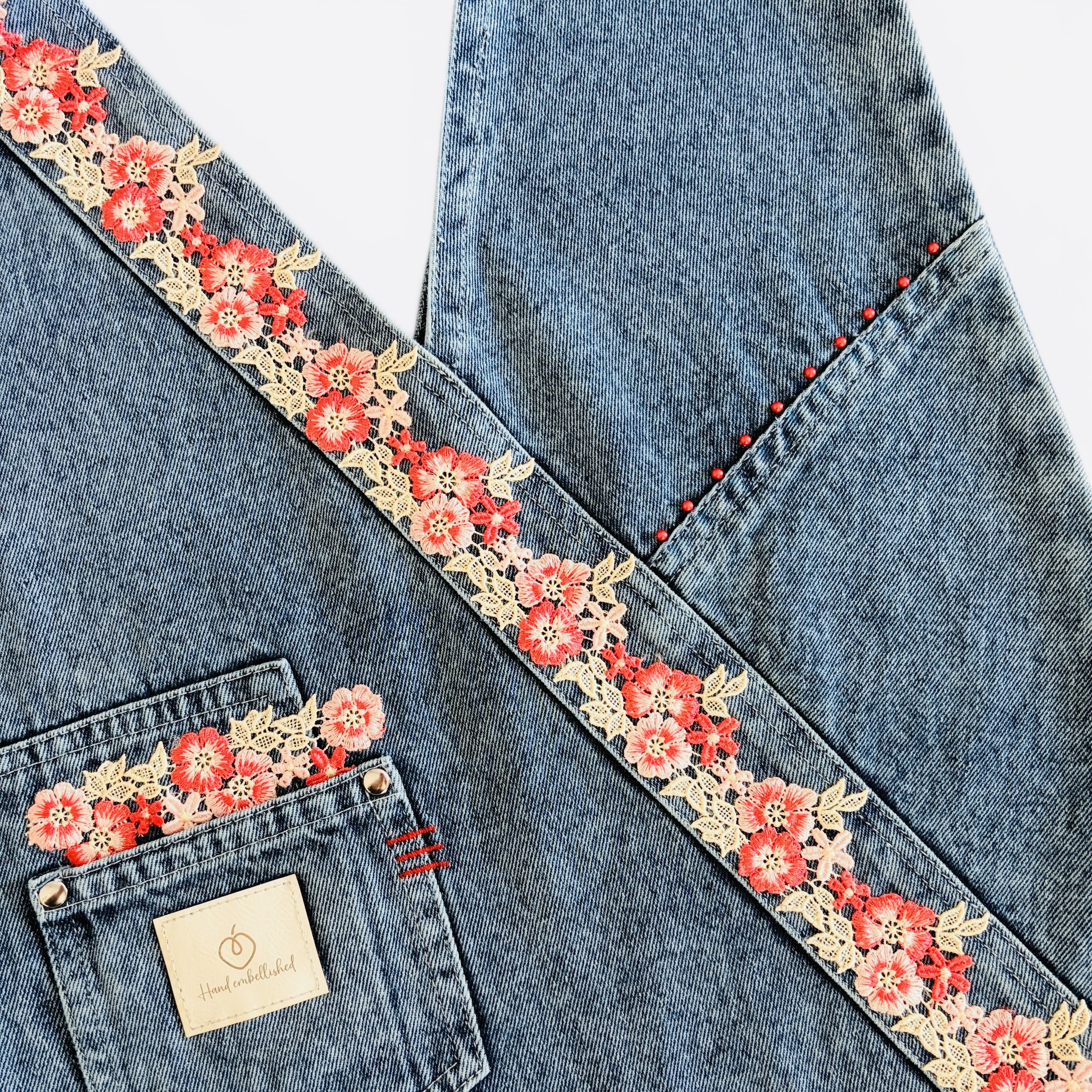 Hand-embellished denim wrap bag with red floral lace, decorative studs and front pocket.