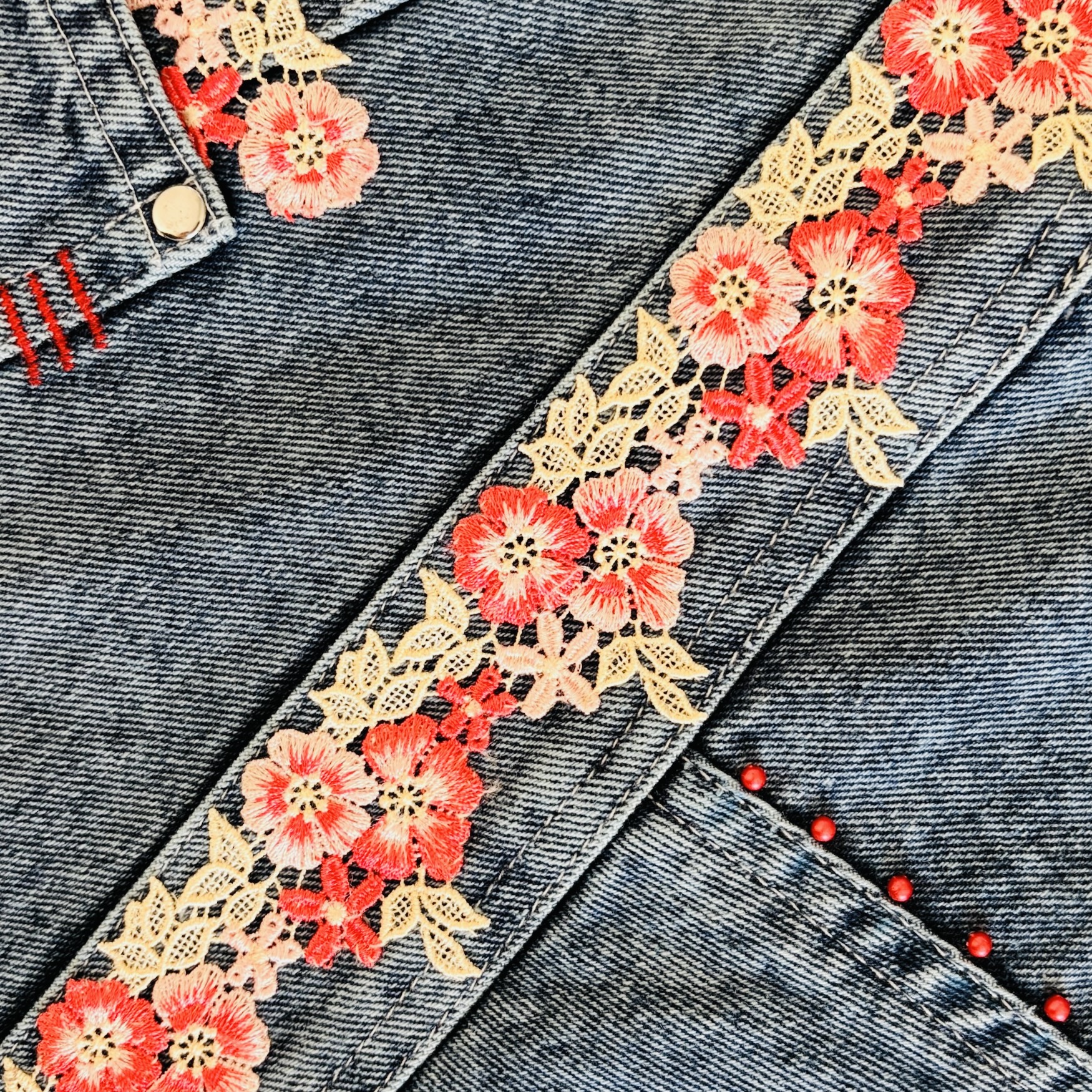 Close-up of red and coral floral lace embellishment on a denim wrap bag.