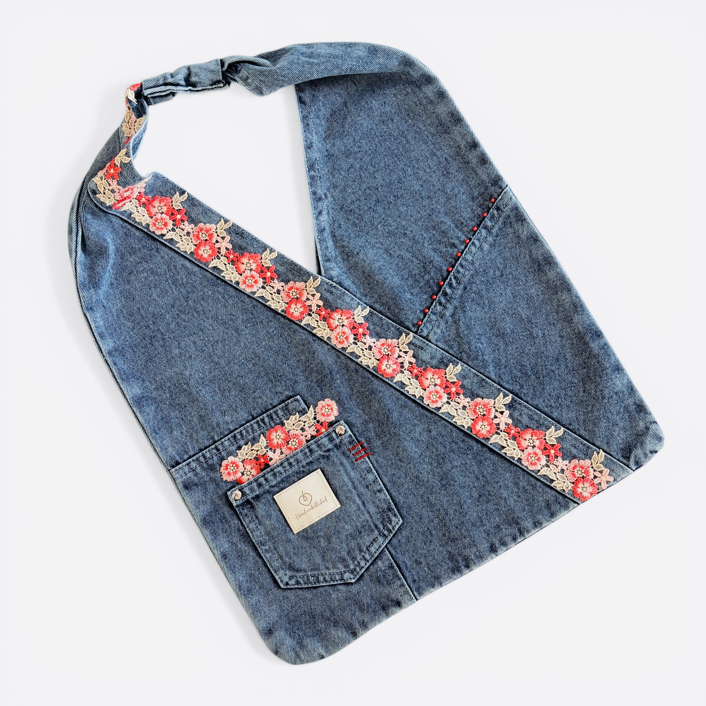Denim wrap shoulder bag with red floral lace embellishment laid flat.