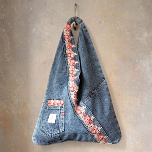 Front view of denim wrap bag with red floral lace hanging from a hook.