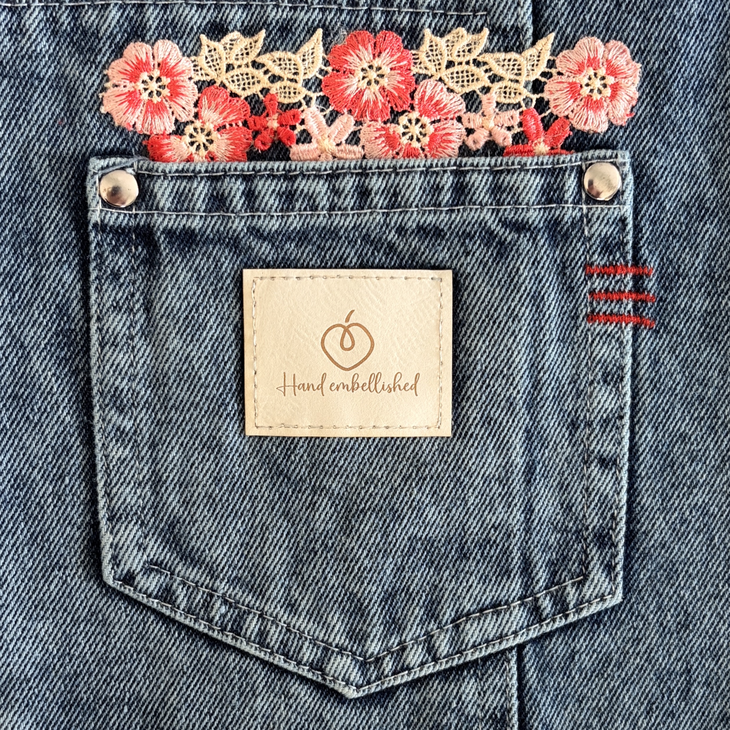 Close-up of denim front pocket with red floral lace and hand-embellished label.