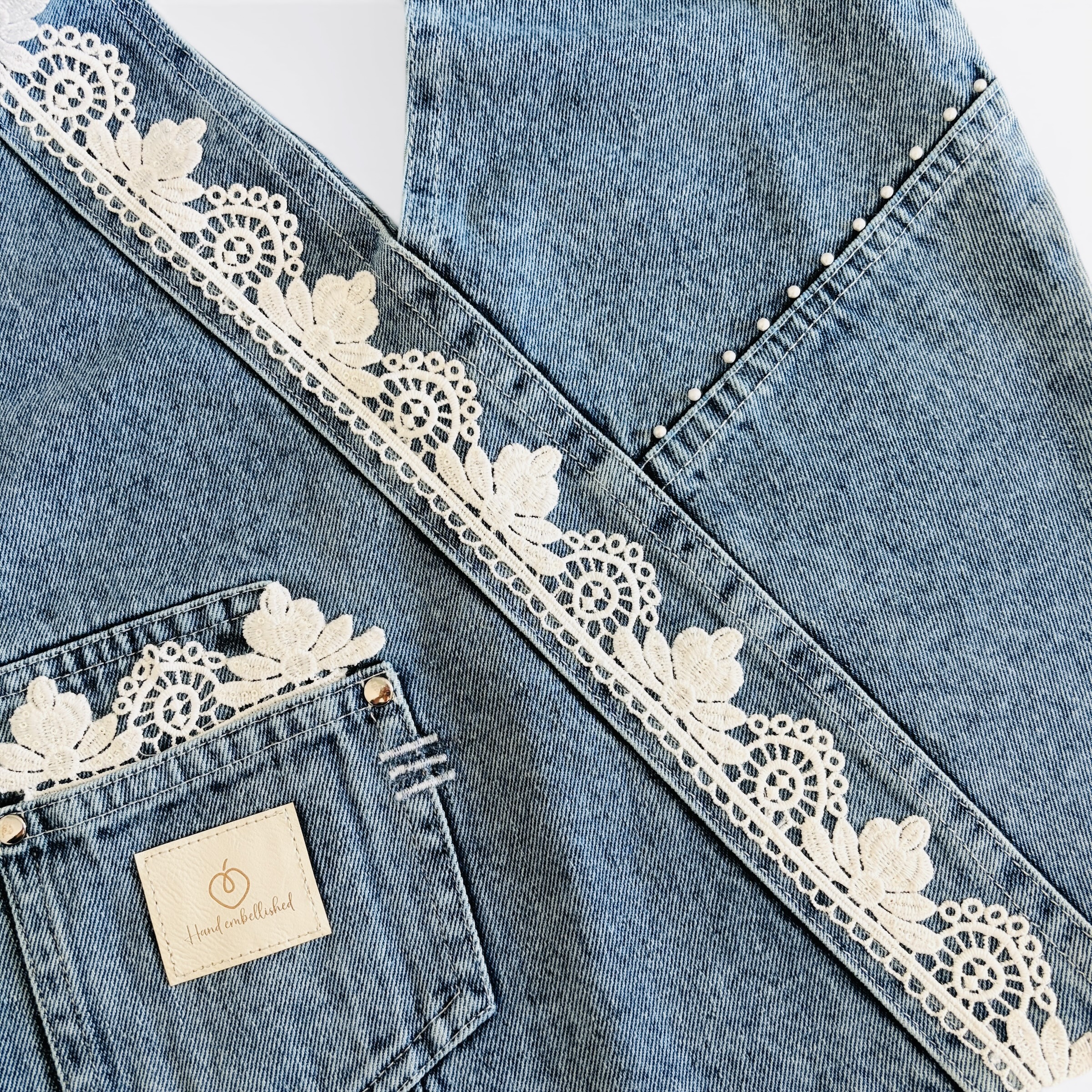 Hand-embellished denim wrap bag with white floral lace trim and front pocket.