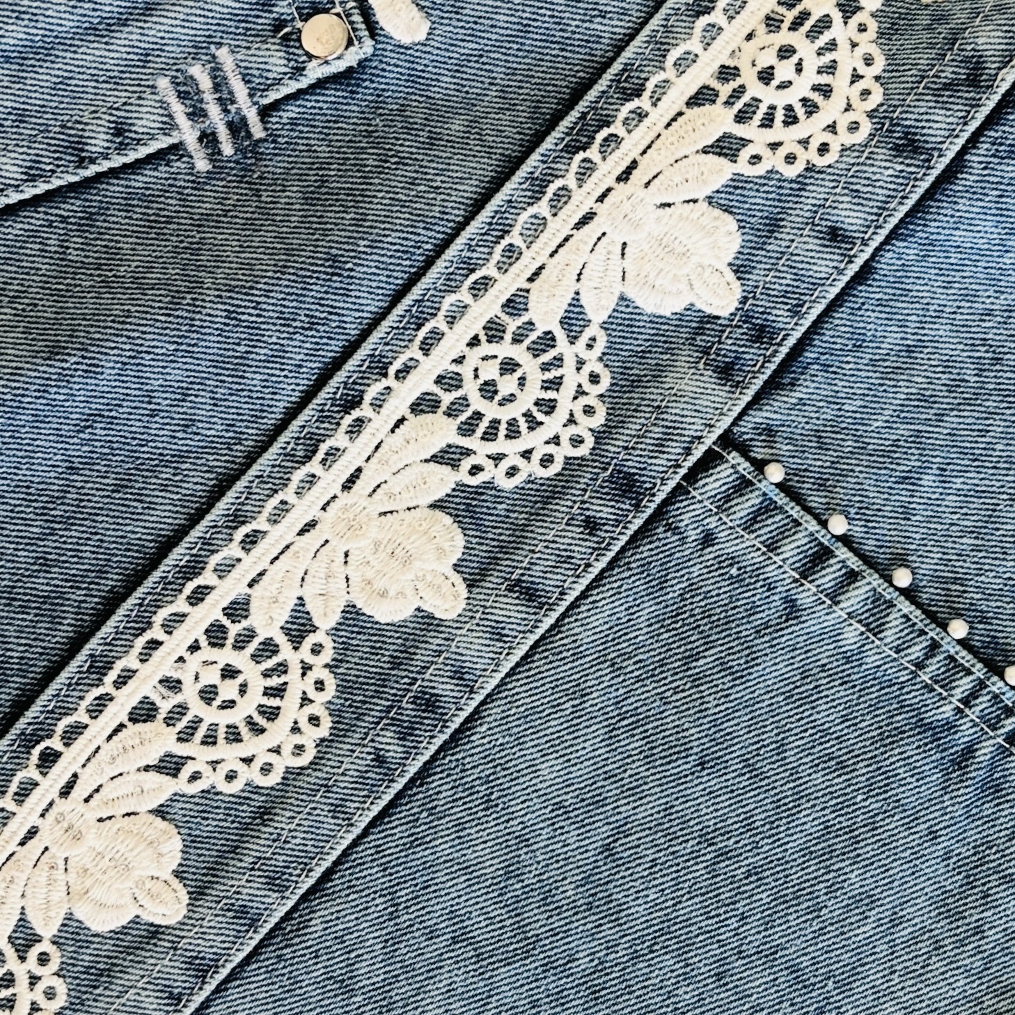 Close-up of white floral lace embellishment on a denim wrap bag.