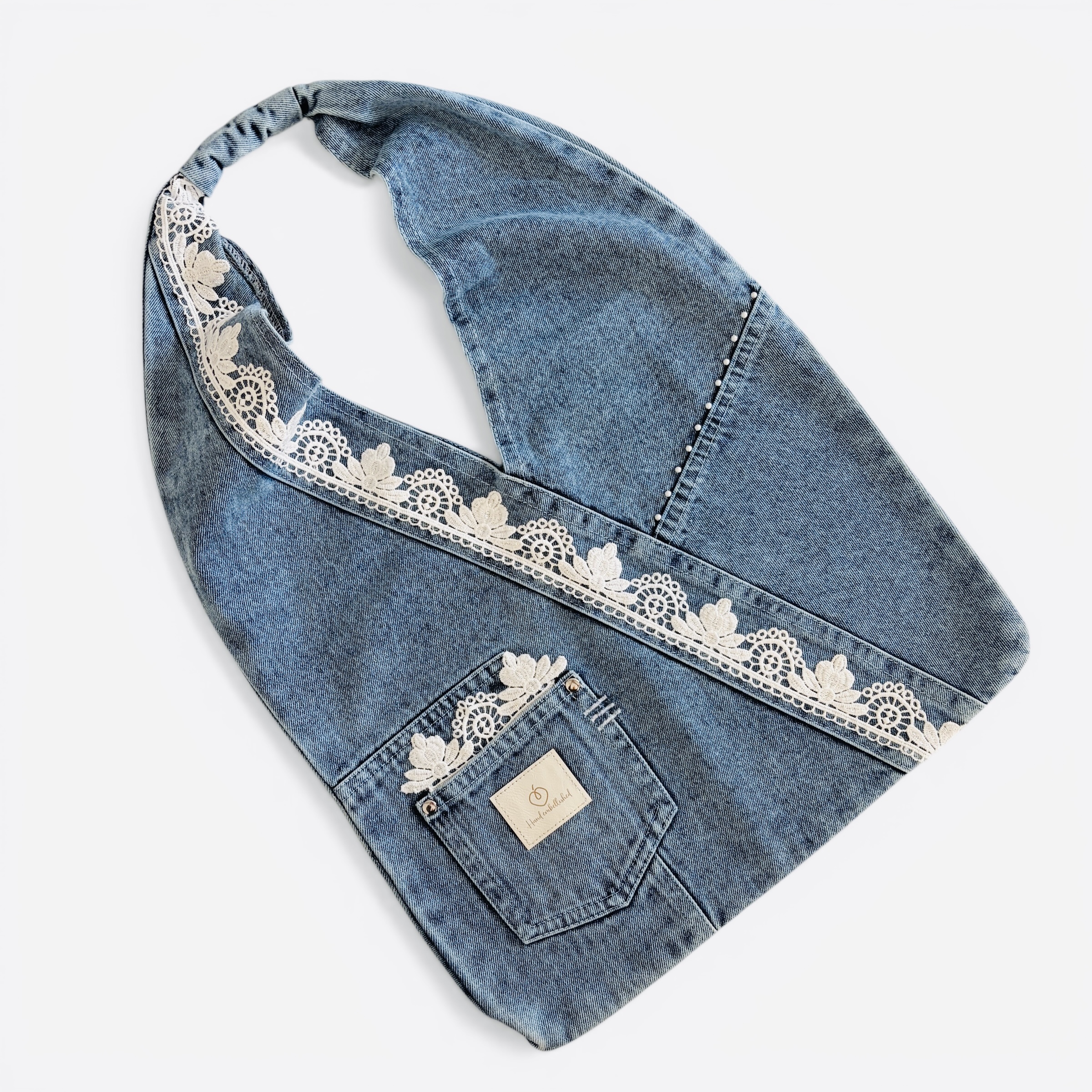 Denim wrap shoulder bag with white floral lace trim laid flat.
