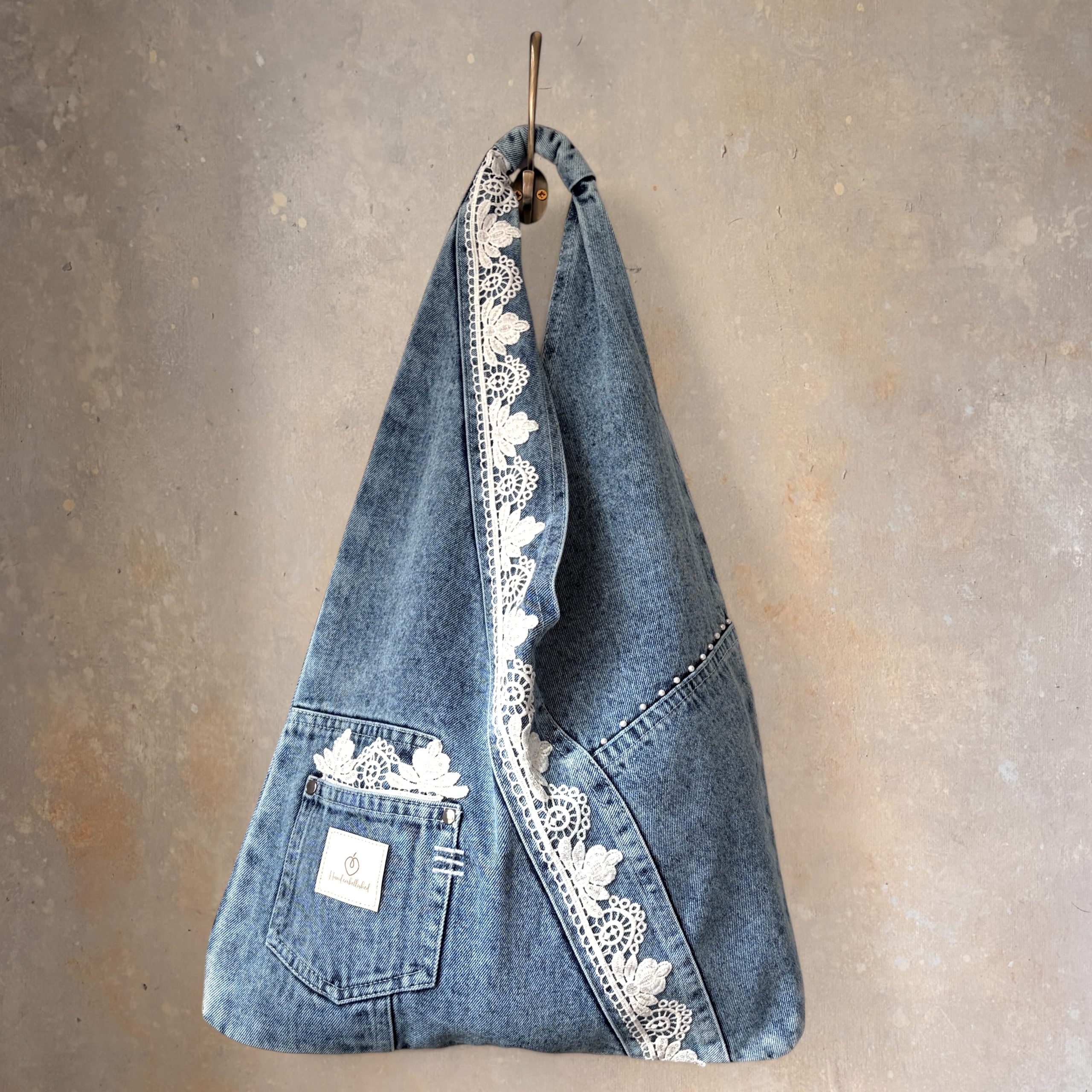 Front view of denim wrap bag with white lace trim hanging from a hook.