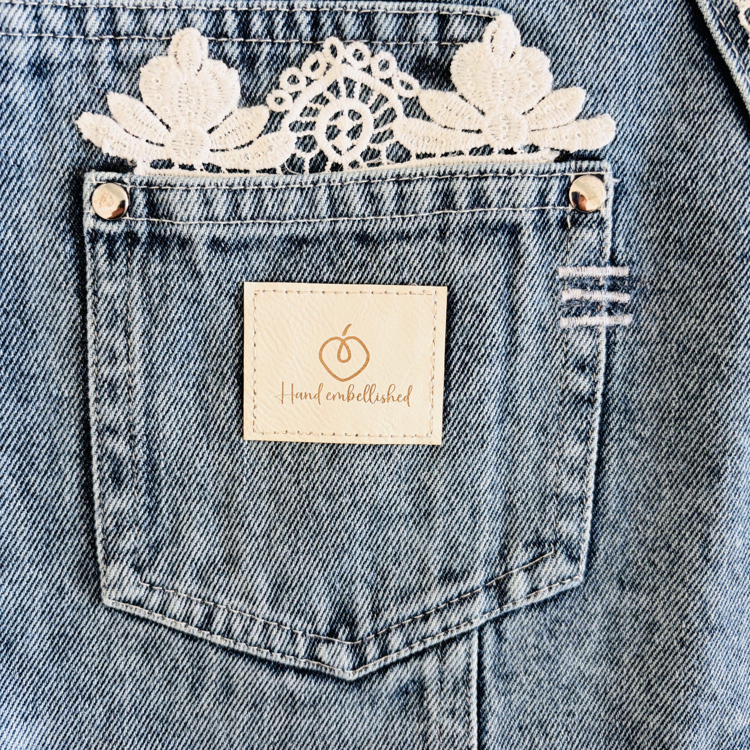 Close-up of denim front pocket with white lace trim and hand-embellished label.
