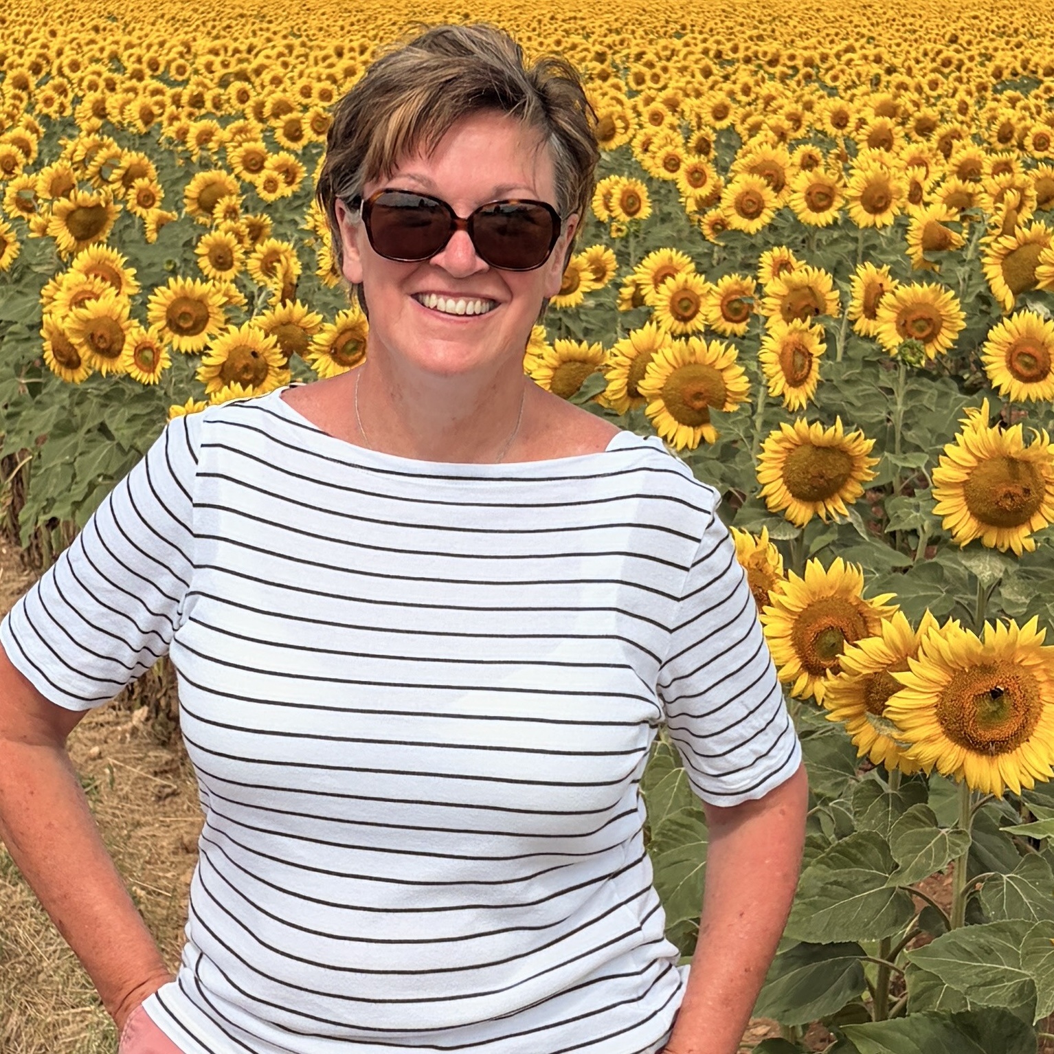 Anne-Marie Fowler, founder of Pomme d'Or, smiling in front of a sunflower field in France.
