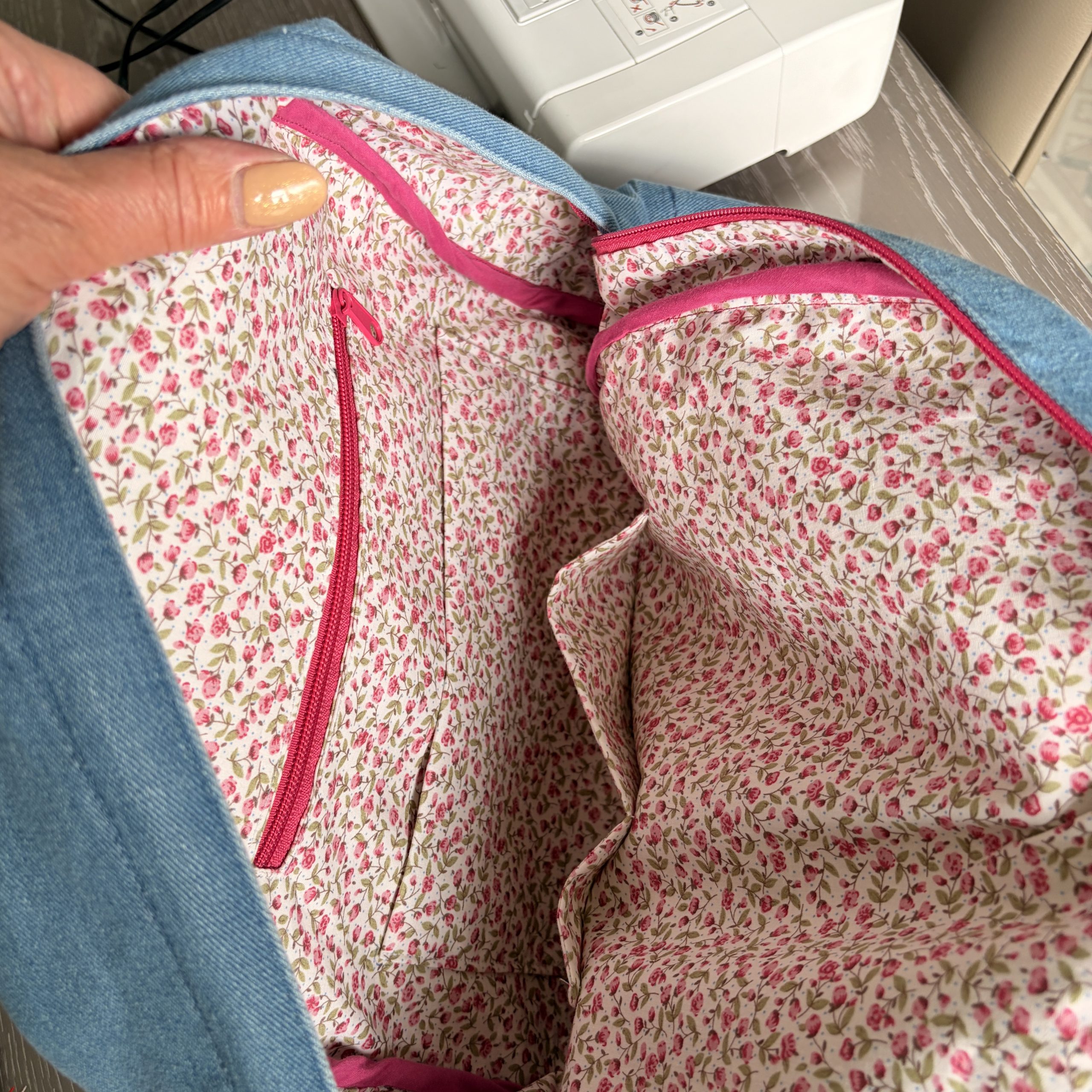 Inside the Gaia denim backpack showing the floral cotton lining and pink zipped pockets