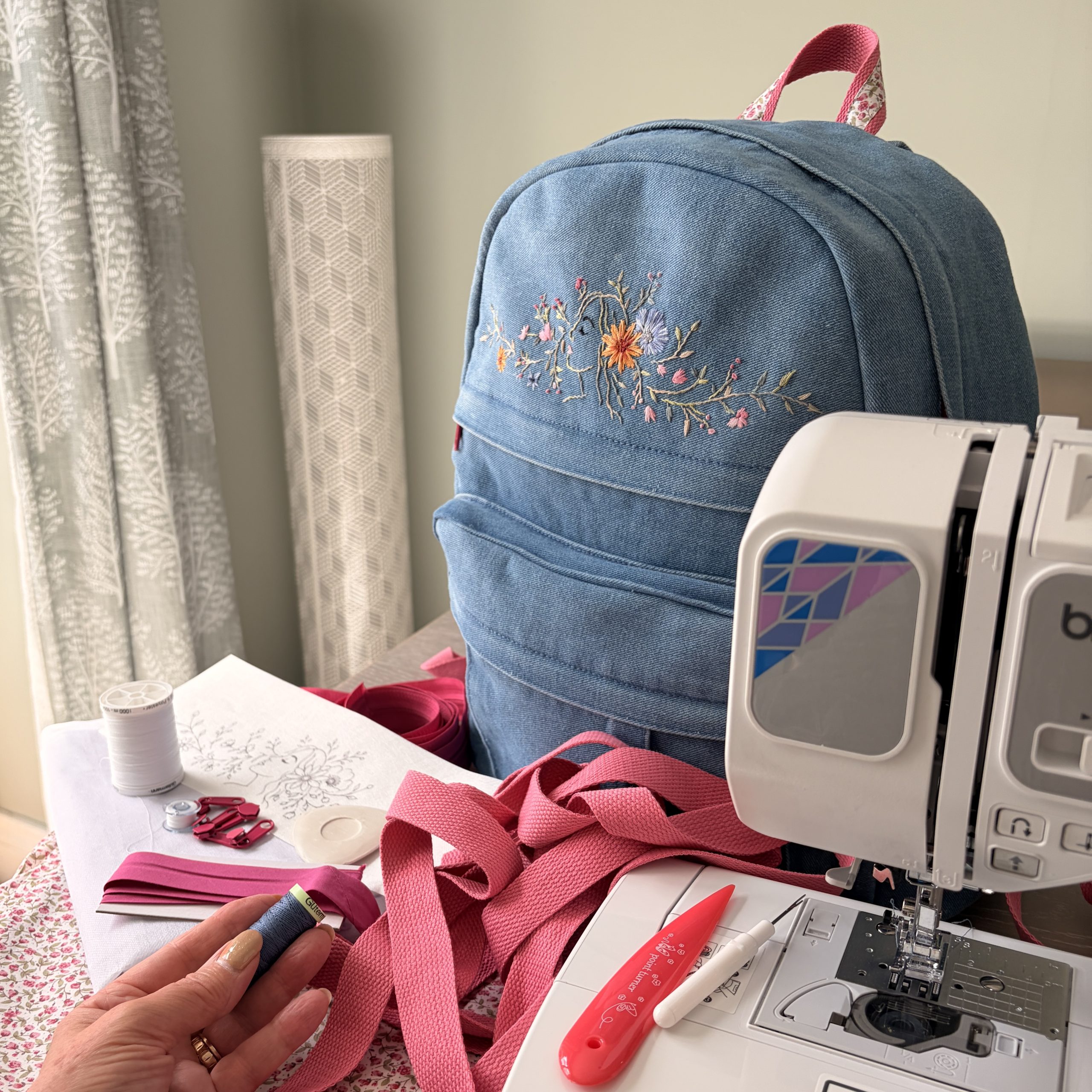 Gaia denim backpack being reworked beside a sewing machine with pink webbing and sewing materials