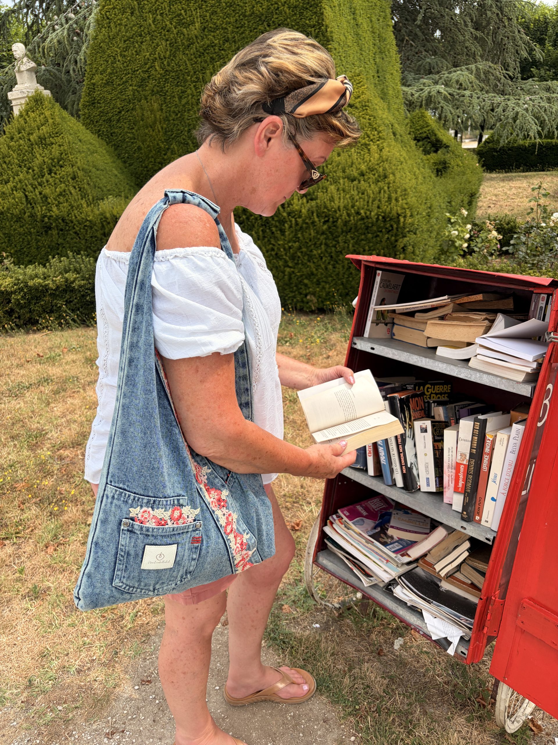 Rosie denim shoulder bag with floral detail being worn beside a book exchange in France
