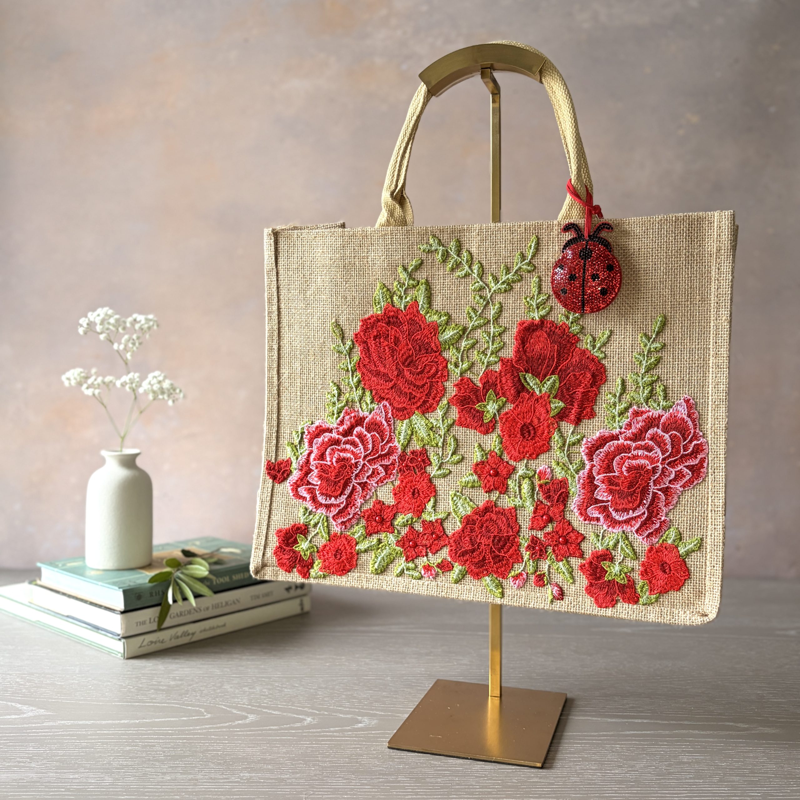 Red floral jute gift bag with embroidered garden flowers and ladybird charm – Pomme d’Or.